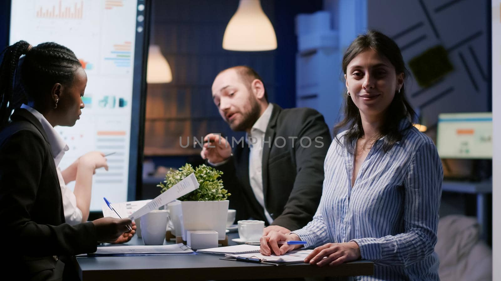 Portrait of businesswoman sitting at conference table in office meeting room working overtime at management ideas. Diverse multi-ethnic teamwork discussing company financial infographics in evening