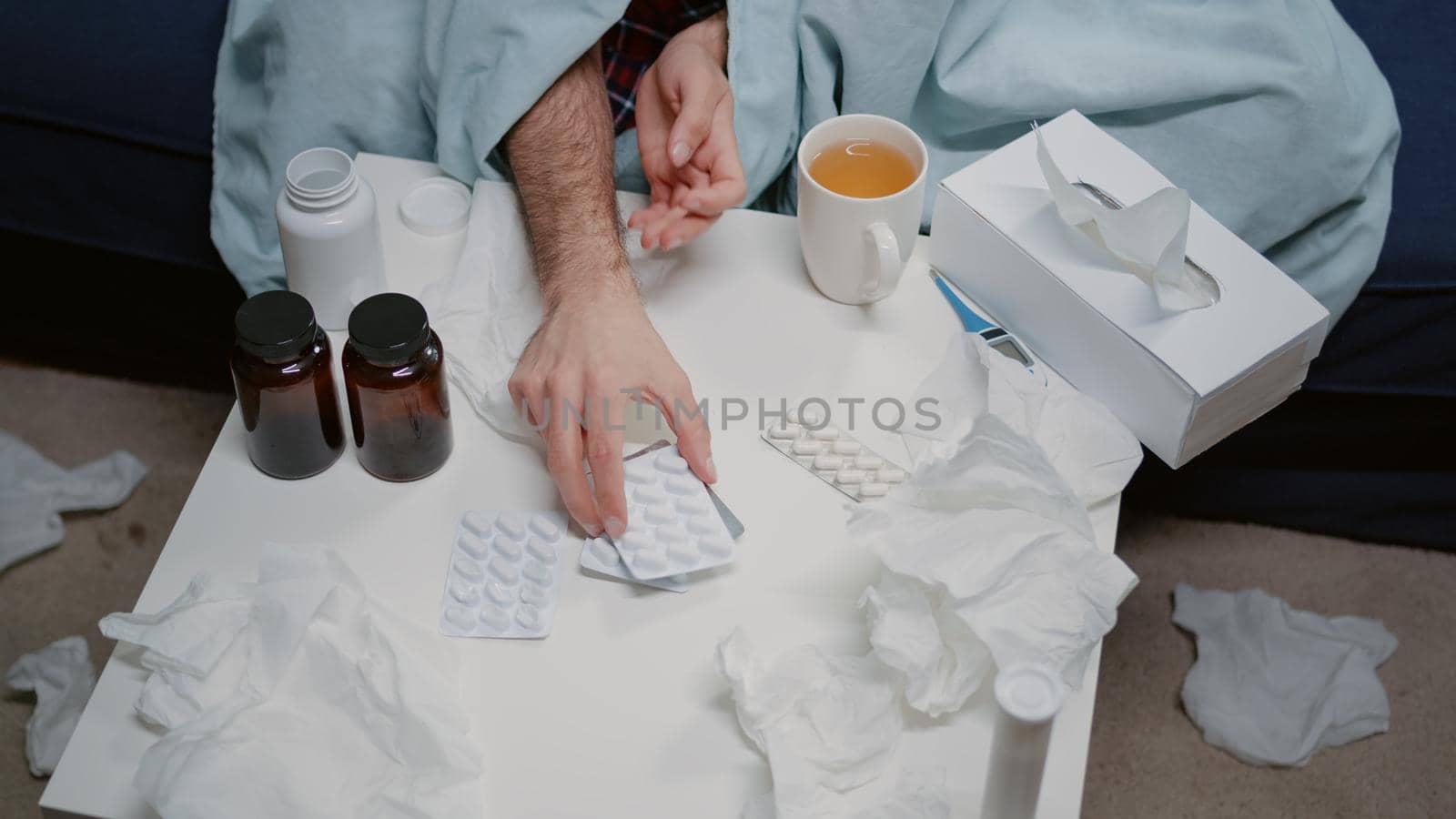 Top view of table with medicaments, bottles of pills and tea for ill man with flu and cold. Sick adult looking at tablets with capsules to cure virus symptoms at home. Person with illness