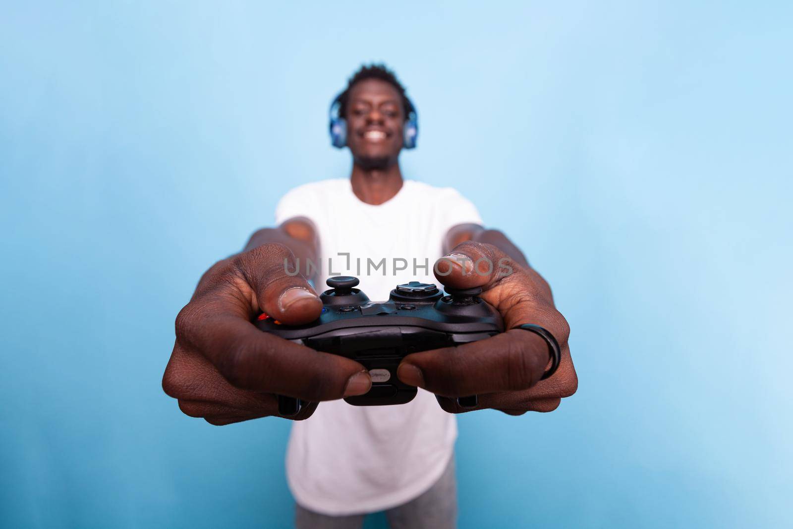 Person showing controller to play video games while wearing headset. Young adult playing game with joystick and listening to music on headphones. Modern man having fun with technology.