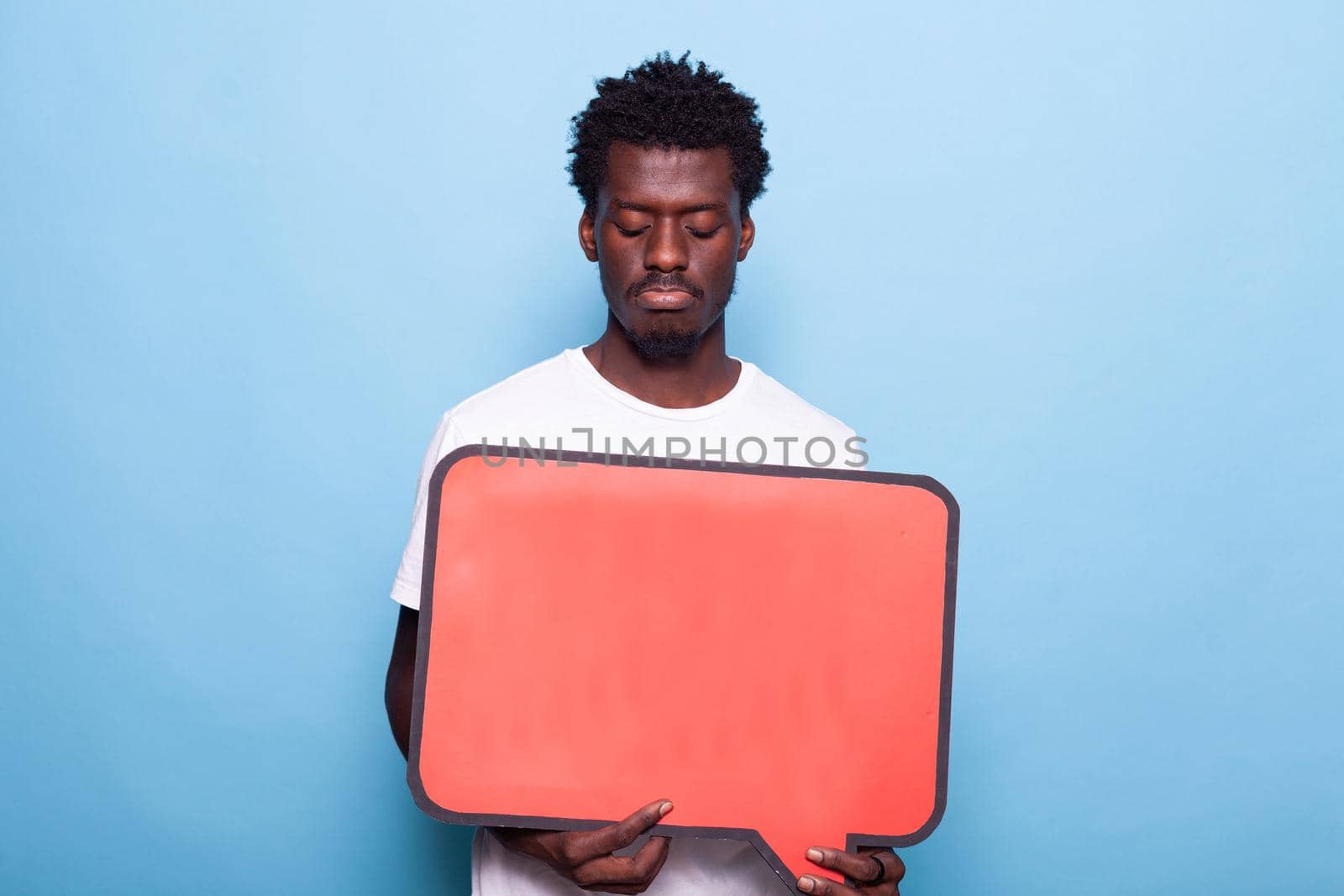 Portrait of young adult holding blank board for communication. Person showing red speech bubble to camera, sign used for written messages and conversation. Man with space for expression