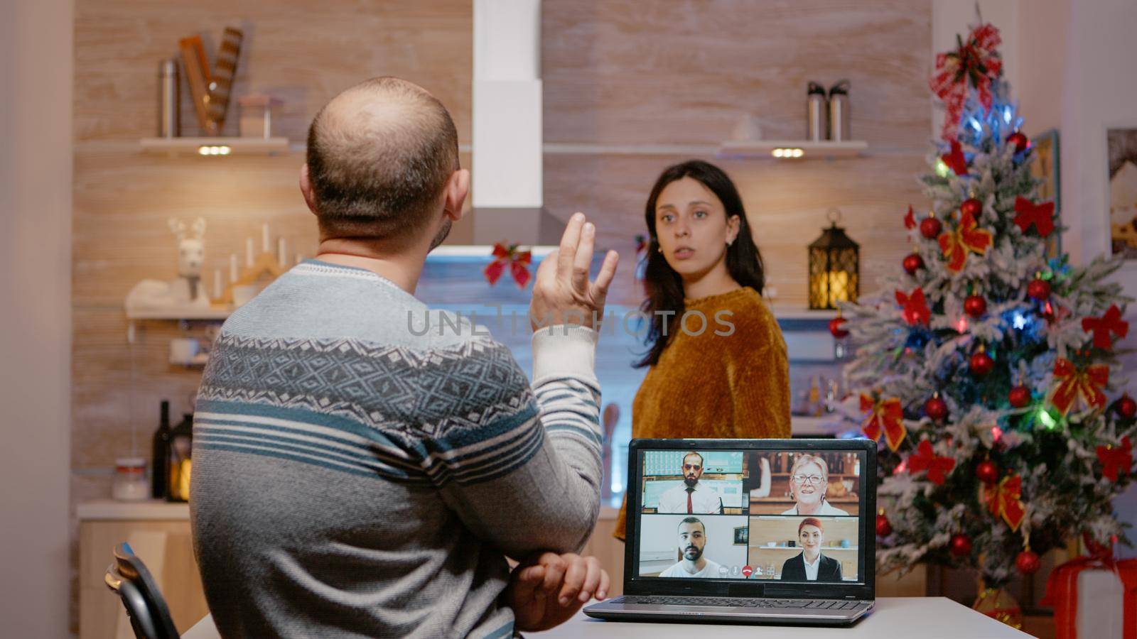 Businessman using video call for work on christmas eve and woman being impatient about celebrating holiday festivity. Husband working from home on laptop while wife preparing for celebration