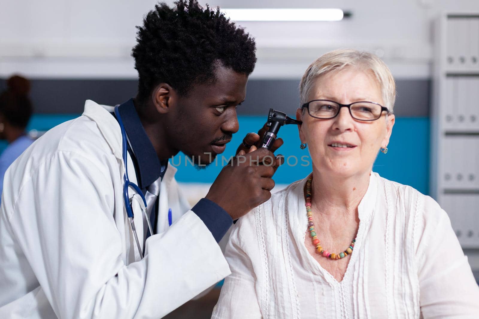 Black young doctor using otoscope on elder patient by DCStudio
