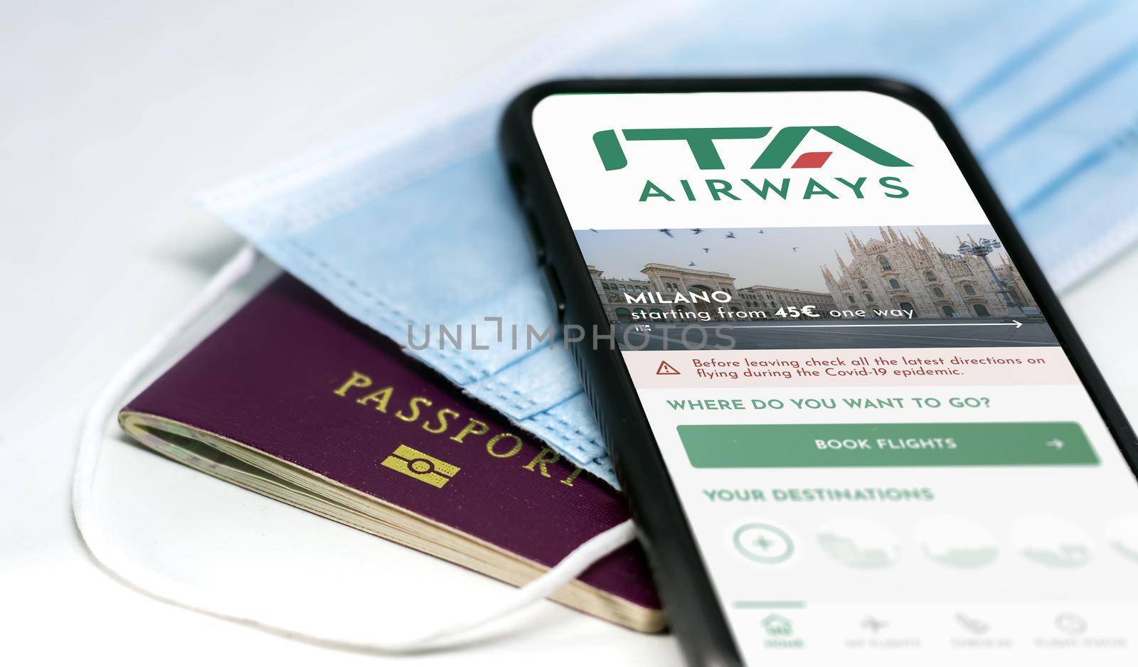 Rome, Italy, October 2021: phone with the ITA Airways app on the screen over a surgical mask and a passport. ITA Airways is the new Italian flag carrier starting from 15 October 2021. Travel safety