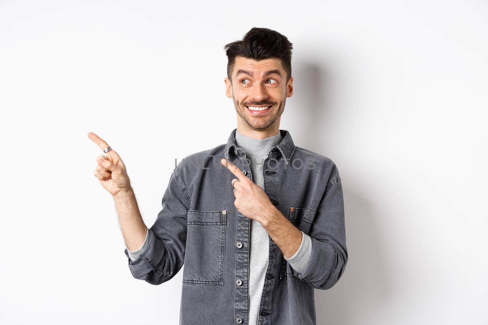 Happy handsome man smiling and pointing left at banner, showing cool product, standing on white background.