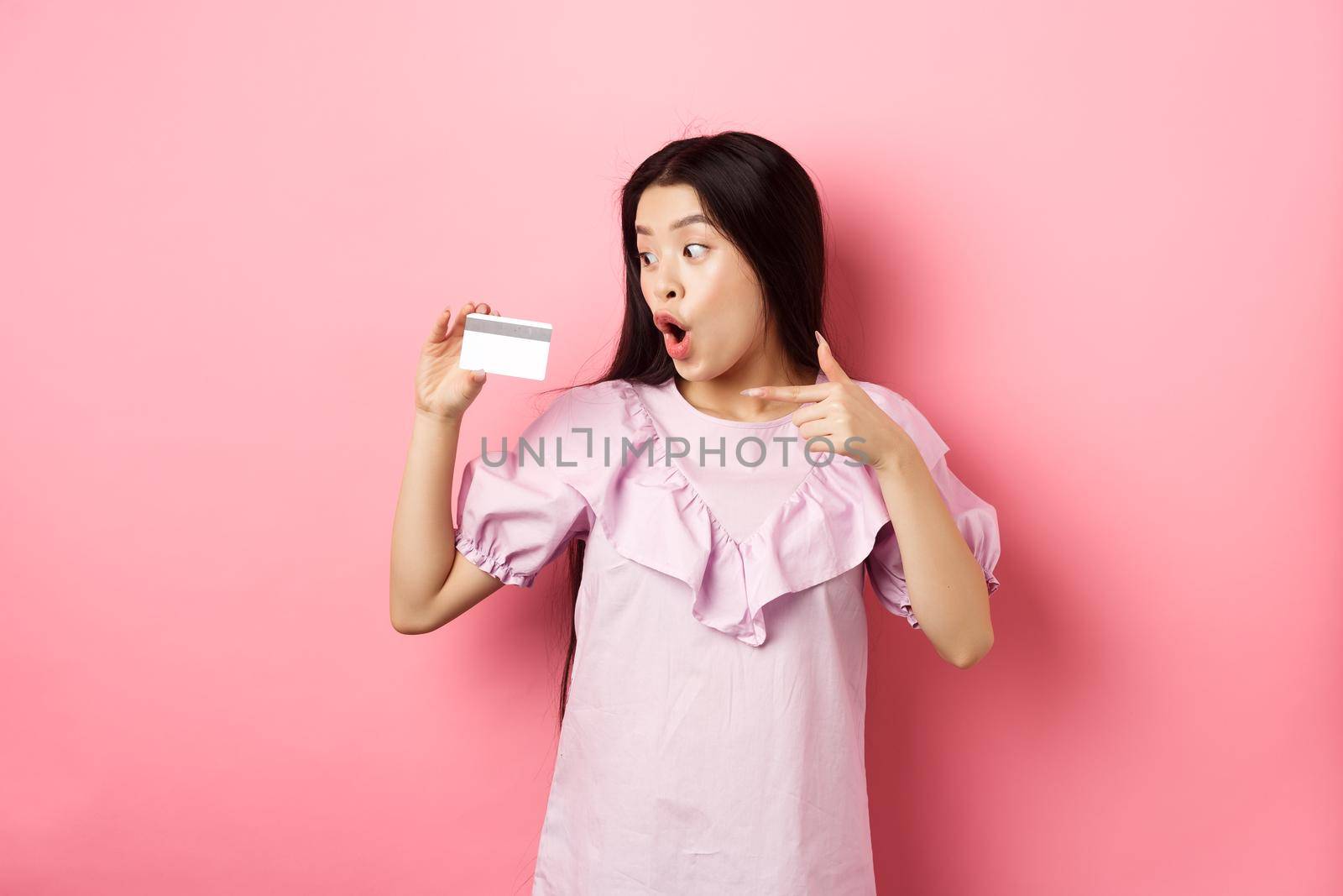 Excited asian woman pointing and showing plastic credit card, gasping amazed, concept of shopping.