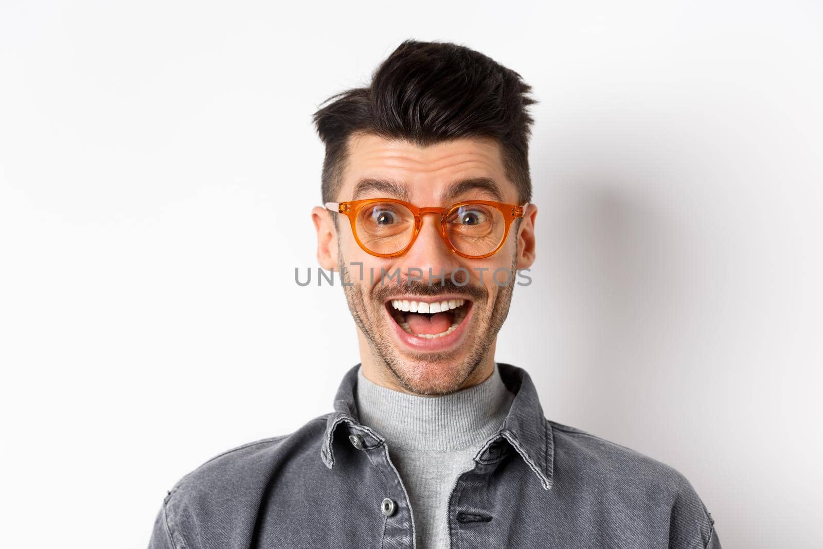 Excited handsome man in trendy eyewear checking out awesome promo, smiling amused, standing happy on white background.