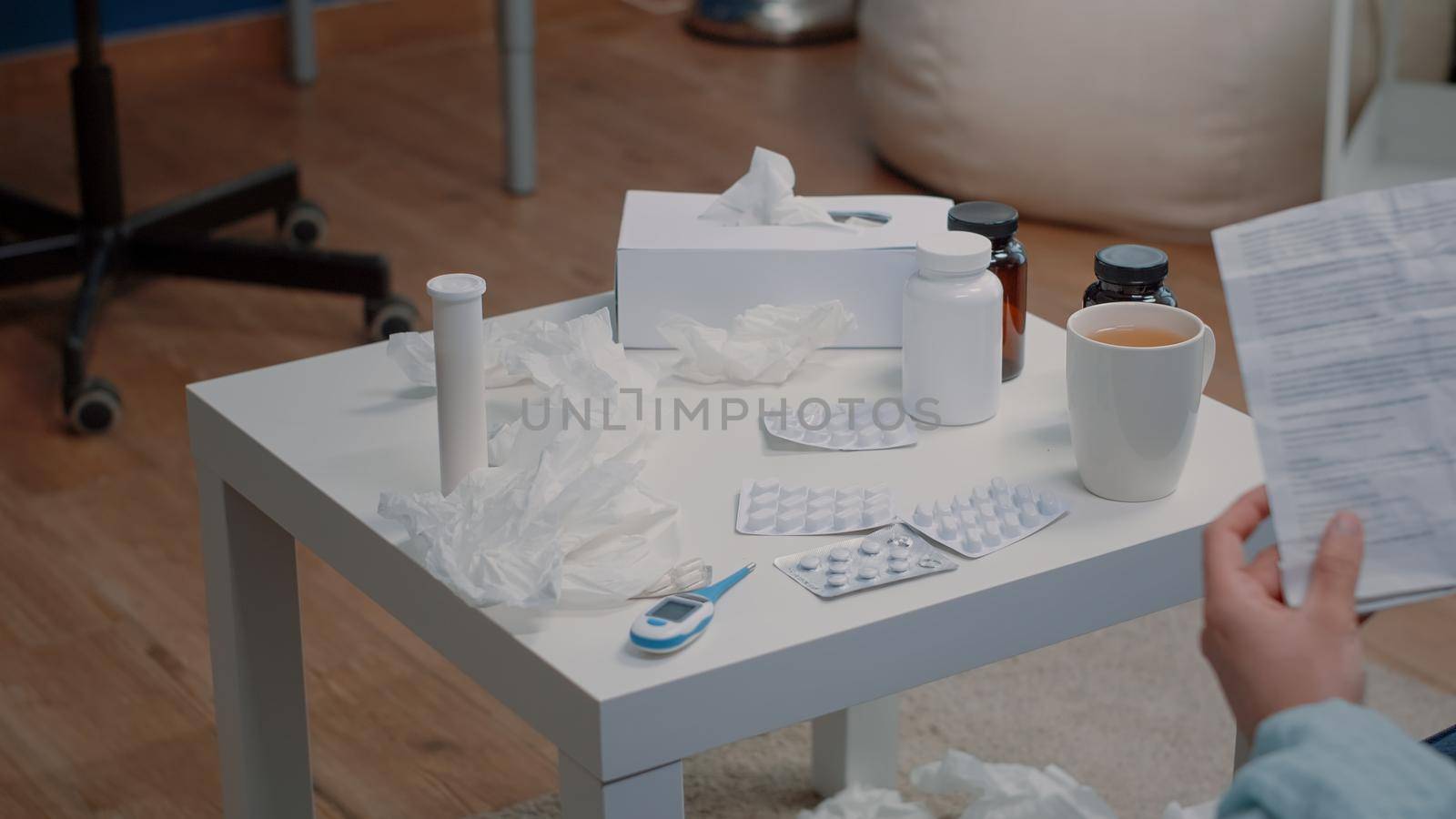 Close up of table with bottles of pills and capsules with tablets while person holding medicine information leaflet to cure disease. Space with medicaments, tea and thermometer