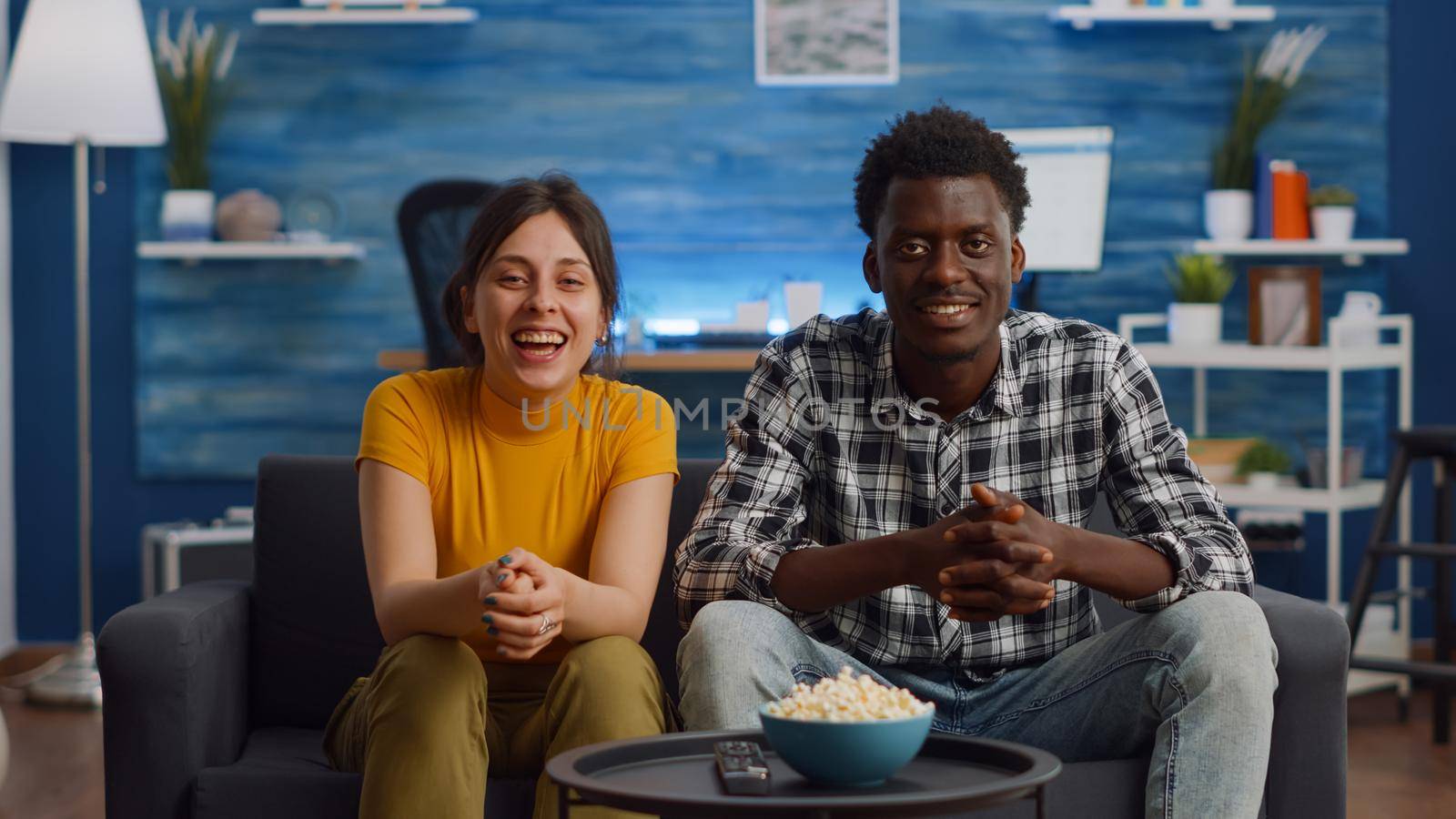 Interracial couple waving at camera on video call conference for remote communication in living room. Young mixed race partners talking to friends on internet online while sitting on sofa.