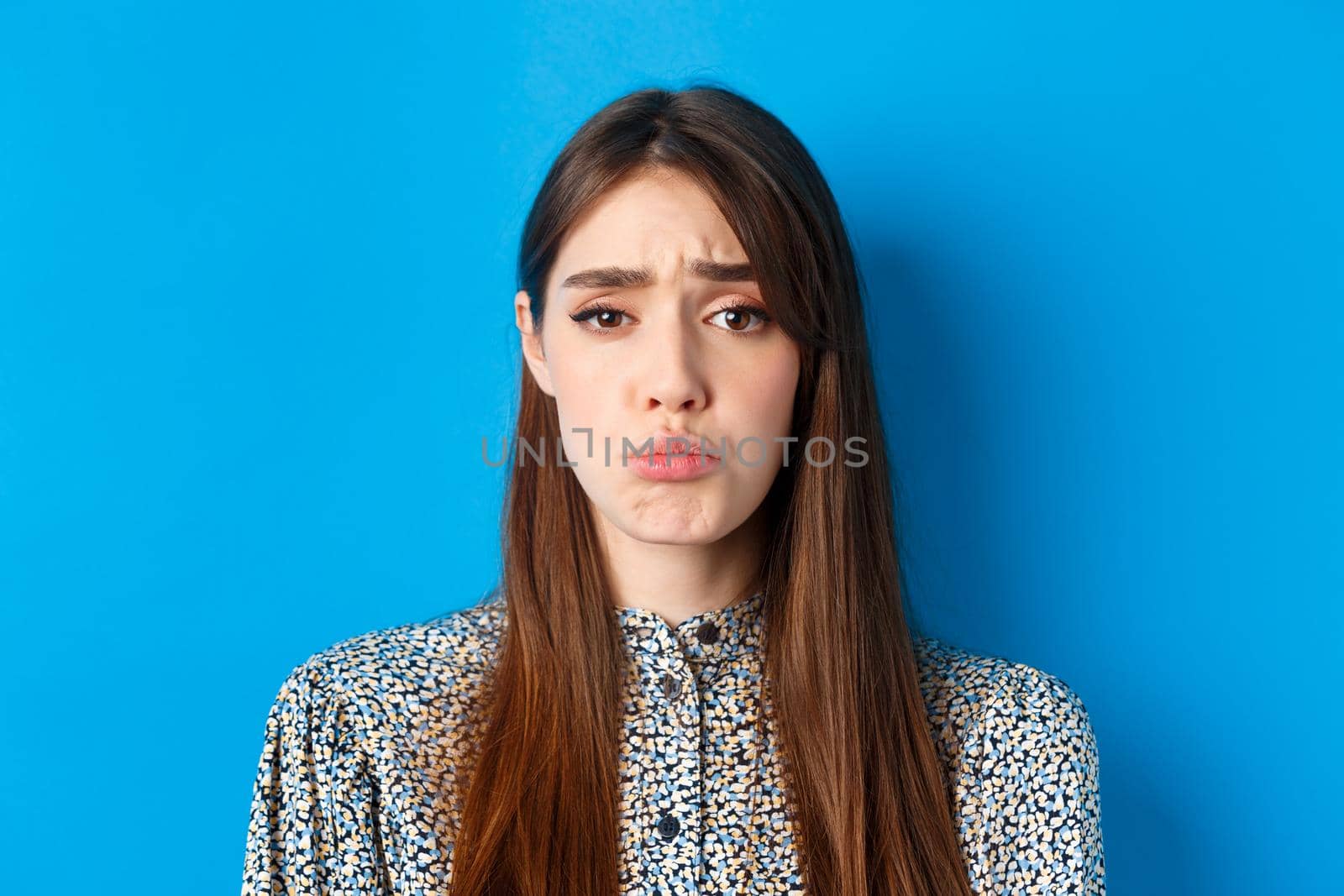 People emotions concept. Sad cute girl begging for something, pucker lips and frowning, whining asking please, standing on blue background.