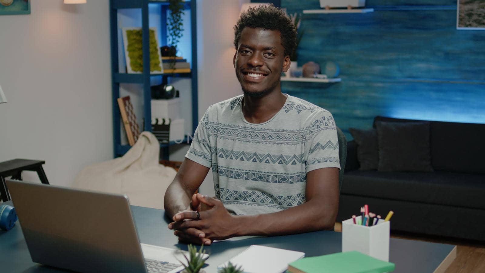 African american man smiling and working on laptop while looking at camera. Portrait of business person sitting at desk with notebook and modern device for office work. Black adult