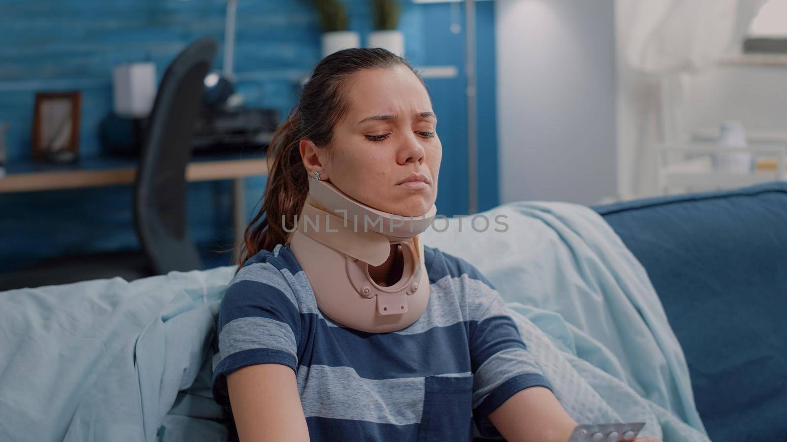 Close up of woman wearing cervical neck foam feeling sick and holding capsule tablet for treatment. Ill adult with medical collar to heal muscle and vertebra injury. Injured person in pain