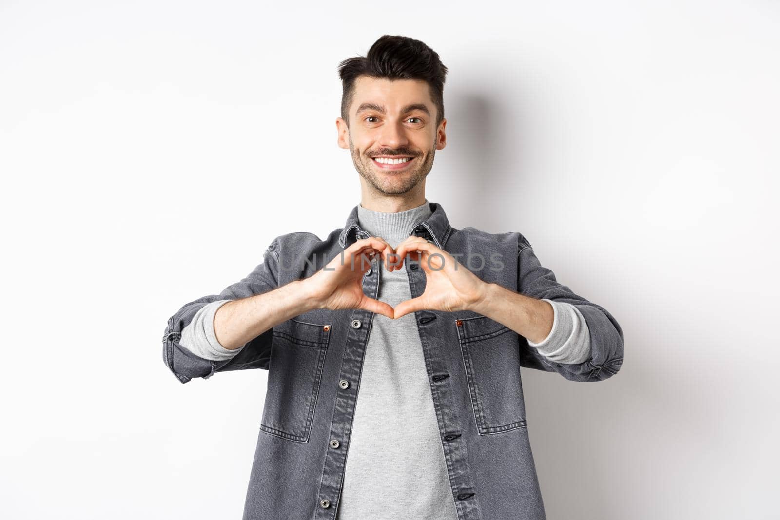 Handsome man showing heart gesture and smiling. Romantic guy say I love you and smiling tender at camera. Valentines day concept.