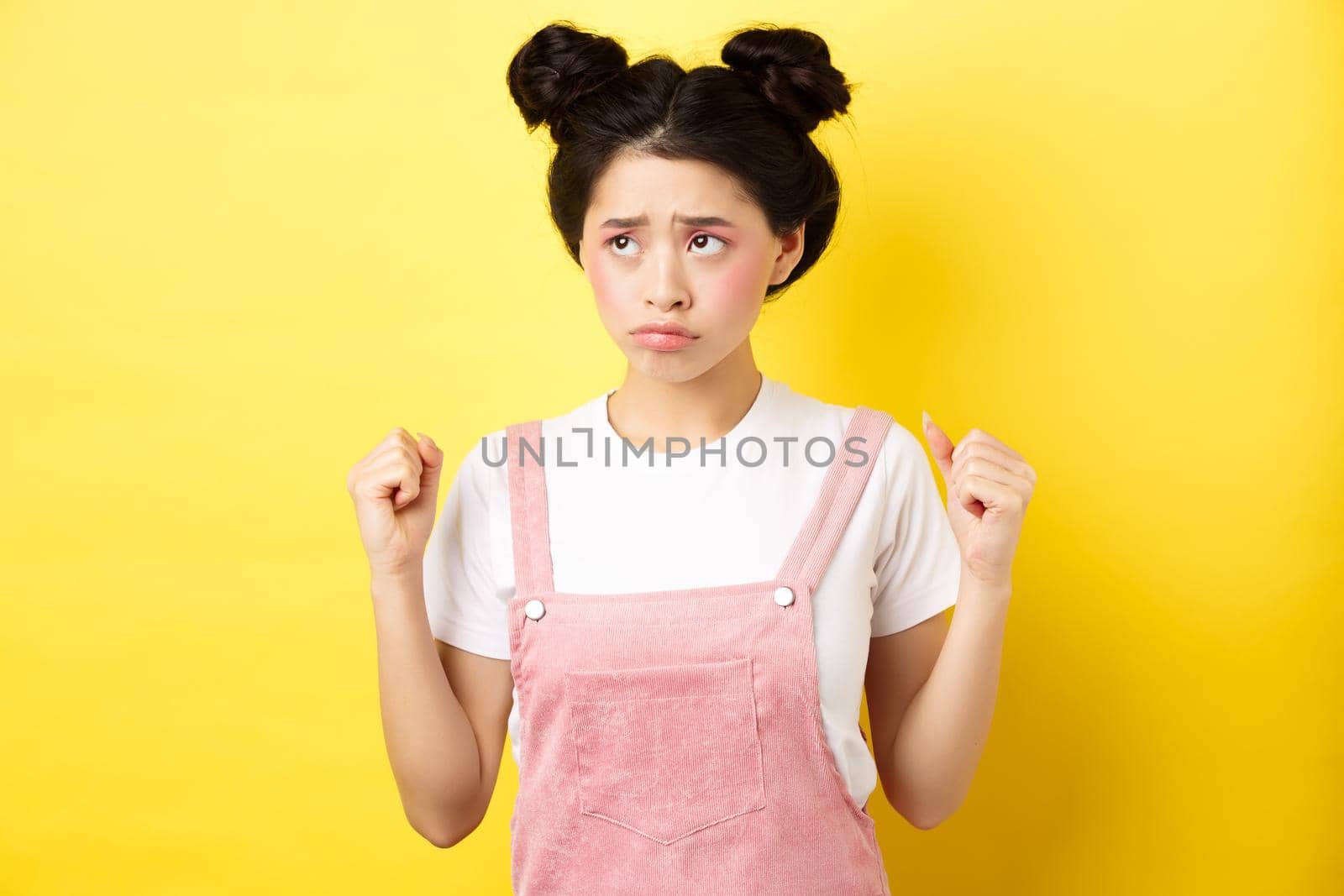 Timid angry girl sulking and clenching teeth, feeling mad but looking cute at upper left corner, standing with makeup on yellow background by Benzoix