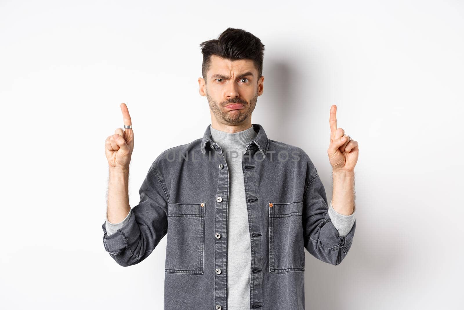 Confused funny guy with moustache pointing fingers up at something strange, frowning and pouting puzzled, standing on white background by Benzoix