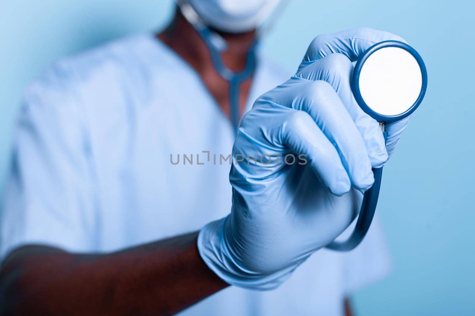 Close up of african american hand holding stethoscope while wearing gloves for healthcare protection. Black nurse with uniform having medical instrument in hand for heartbeat examination