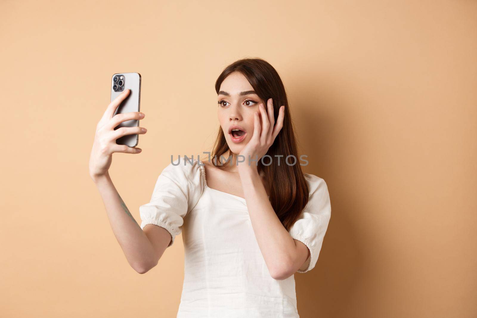 Fashion girl record smartphone blog, taking selfie on cellphone, standing on beige background by Benzoix