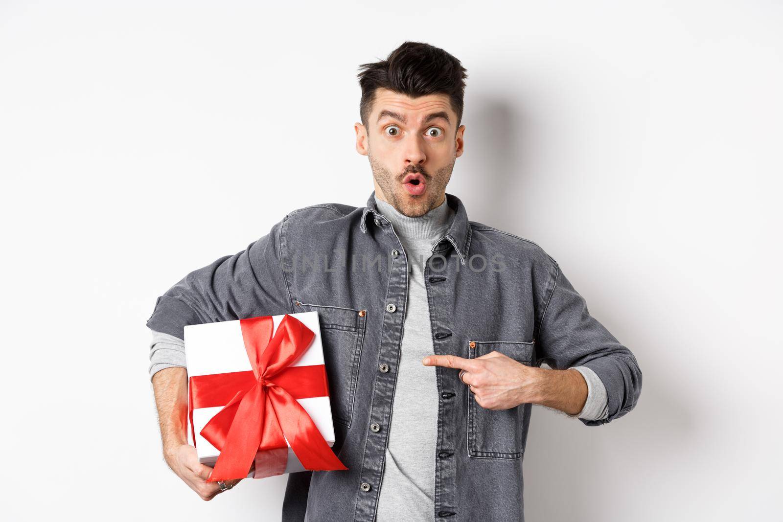Happy Valentines day. Man shopping for romantic date, pointing at gift box and looking amazed, saying wow impressed, showing lover present, white background.