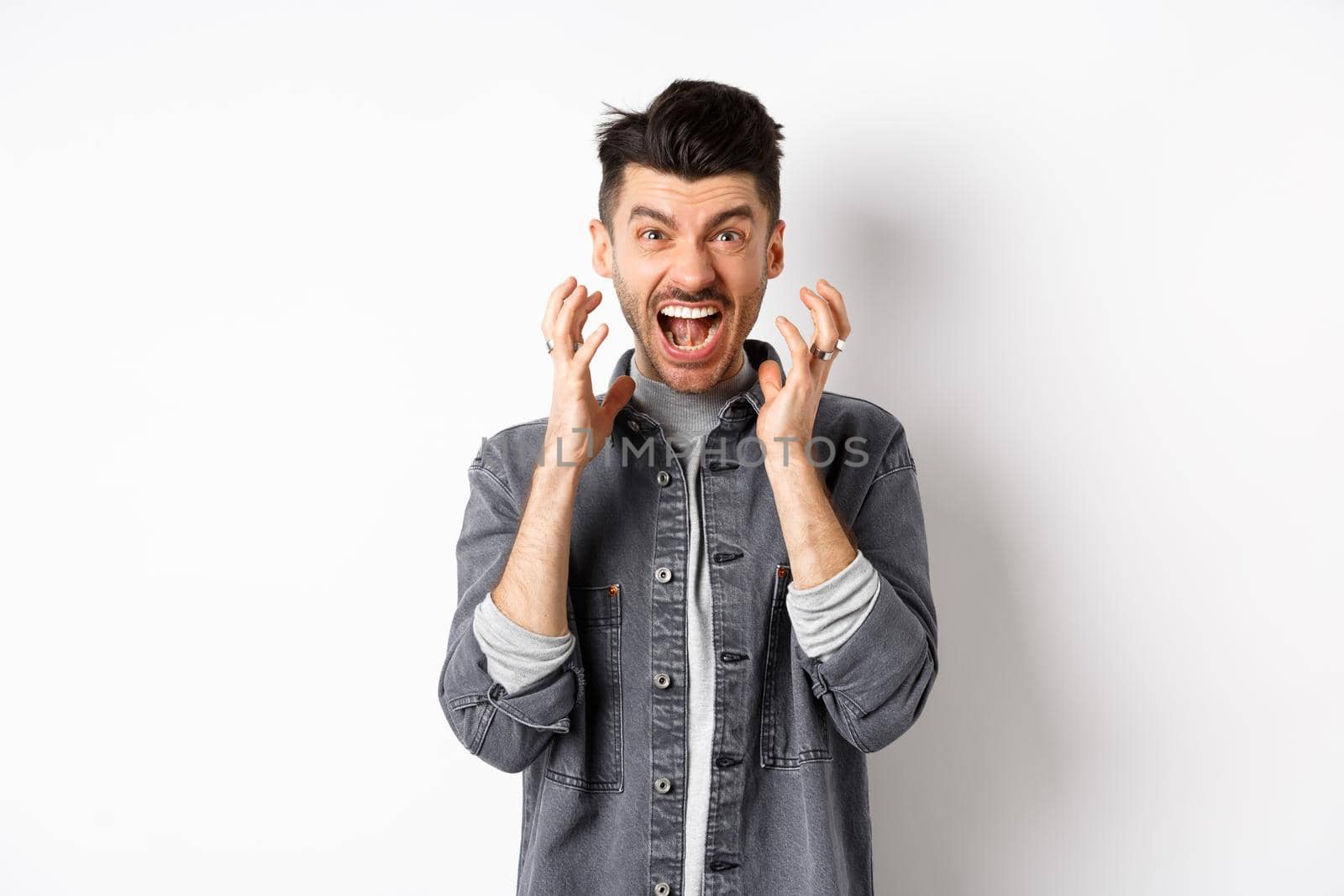 Angry man screaming distressed, losing temper and shouting frustrated, staring at something bad, standing on white background.