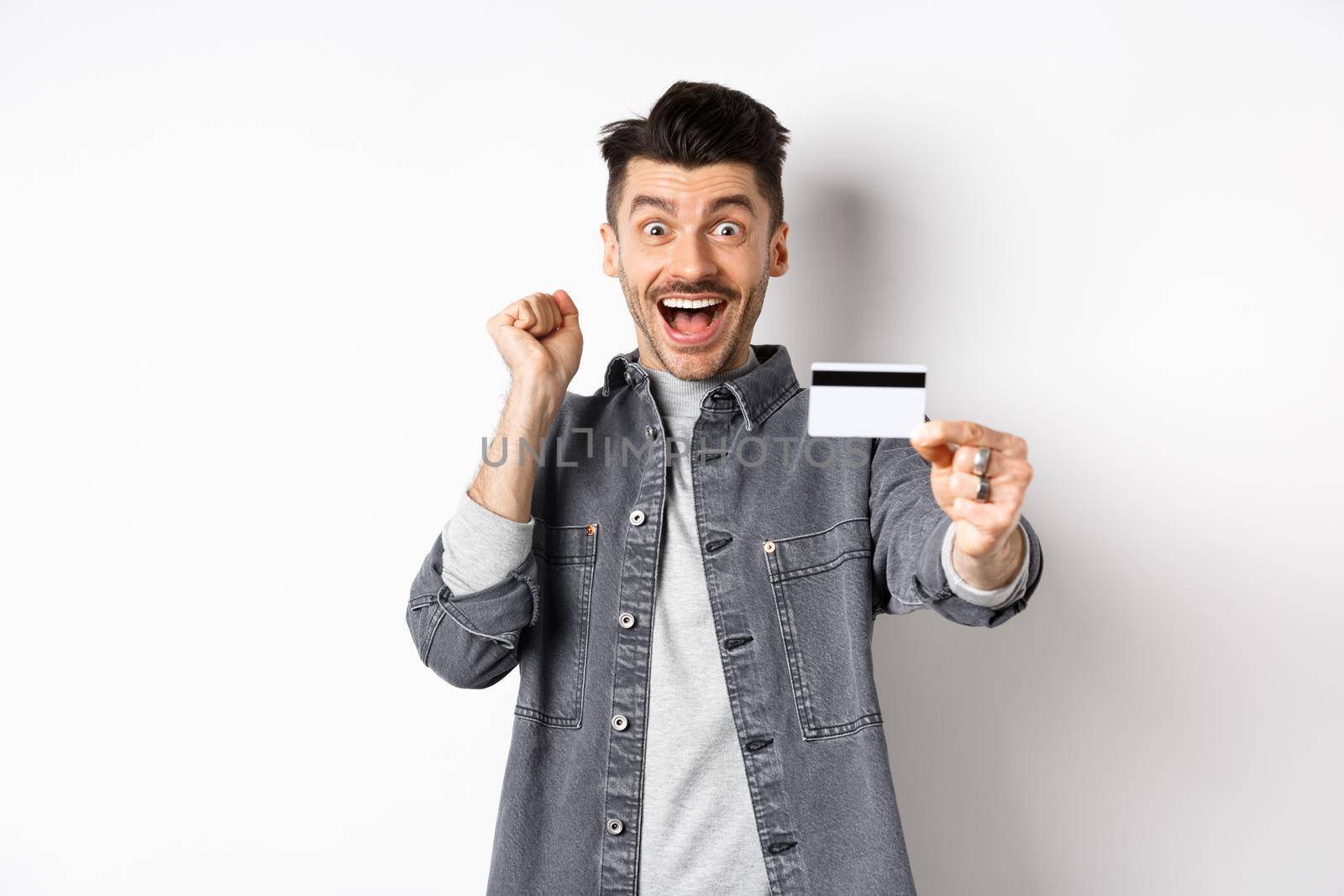 Happy man scream from excitement and show plastic credit card, recommending bank, standing on white background.