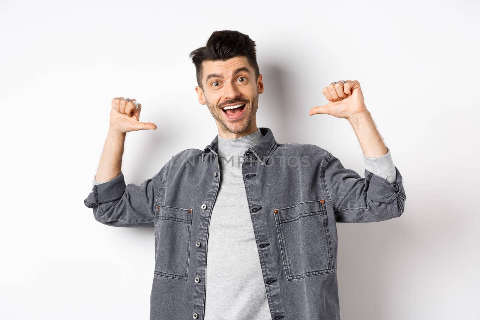 Handsome and confident man smiling, pointing at himself, self-promoting and feeling like professional, standing on white background.