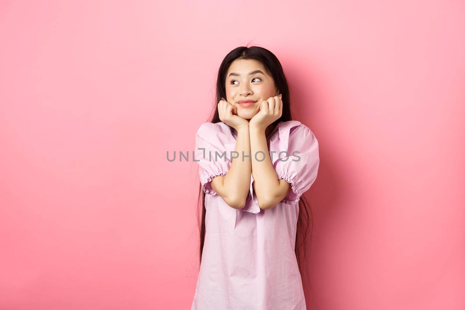 Dreamy romantic girl looking aside at logo and smiling, thinking of something beautiful, standing on pink background by Benzoix