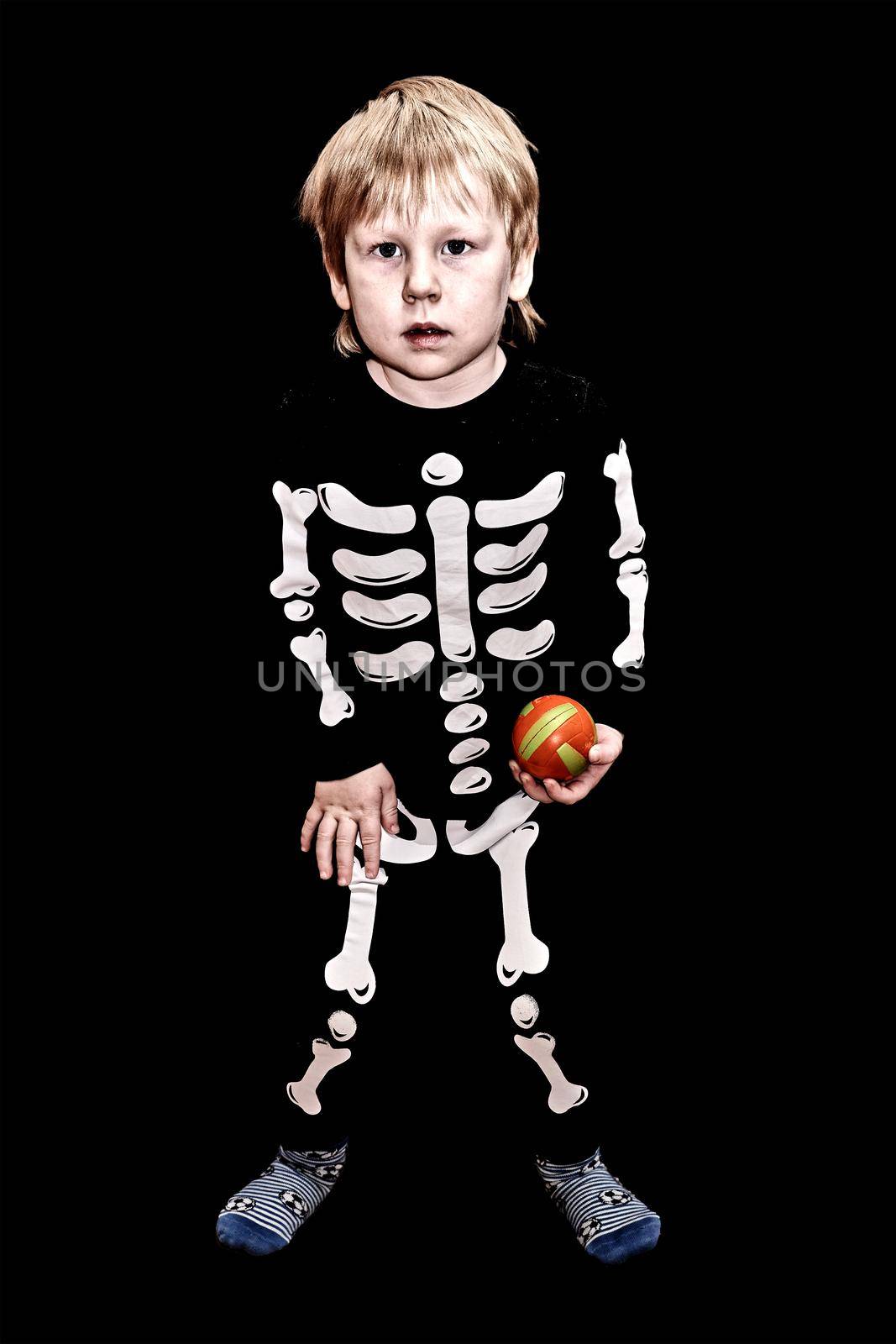 child of four years old in a skeleton costume with an orange ball in his hand on black background. Children fears and scares
