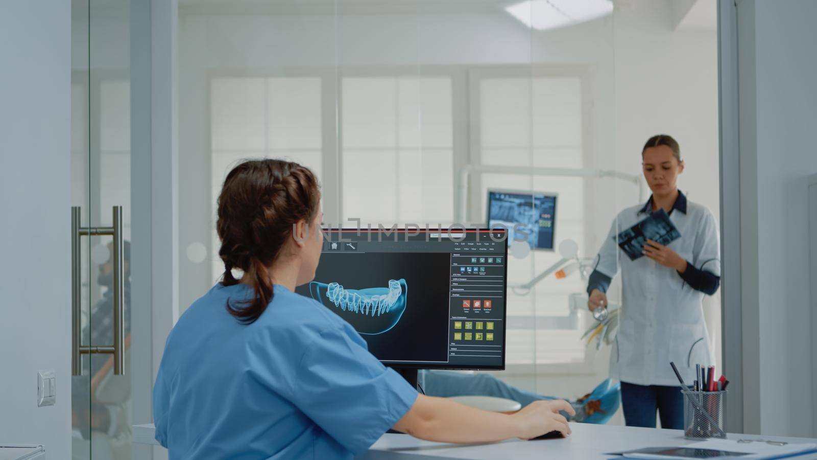Dentistry assistant using computer with virtual teeth animation while giving x ray scan to dentist for patient examination in oral cabinet. Stomatology team with radiography and monitor