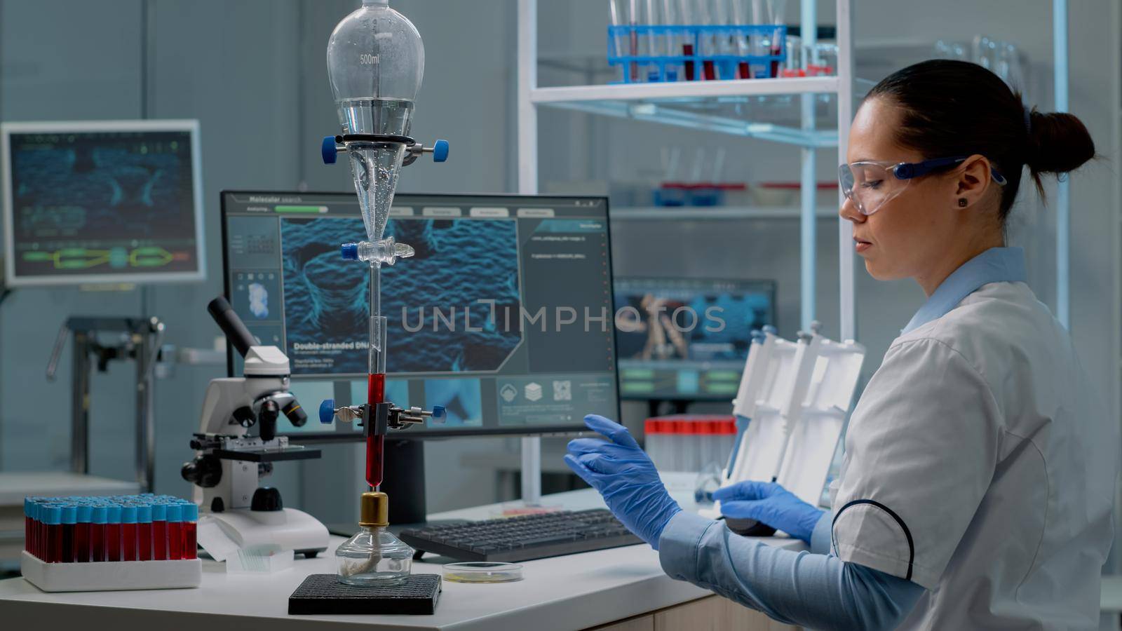 Chemist doctor using animation computer in laboratory while analyzing vacutainers with blood samples. Research specialist with test tube and drip pipe on desk, looking at science monitor