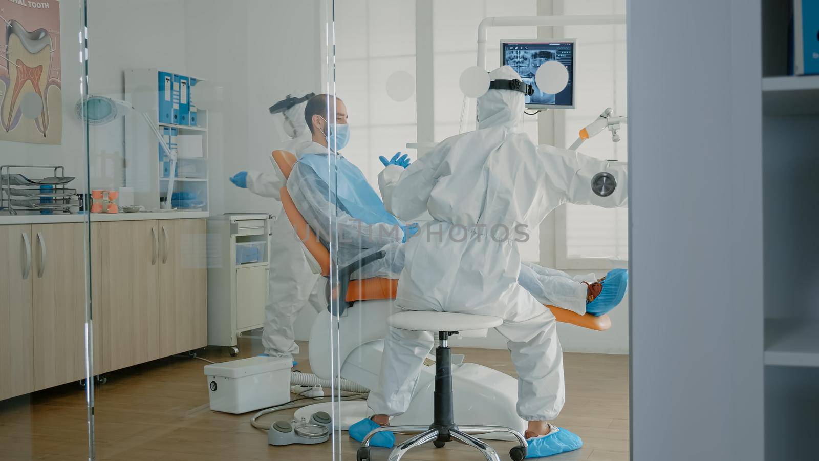 Orthodontists and patient wearing ppe suits in oral cabinet for teeth examination during pandemic. Dentist and assistant using dental equipment and tools for professional consultation