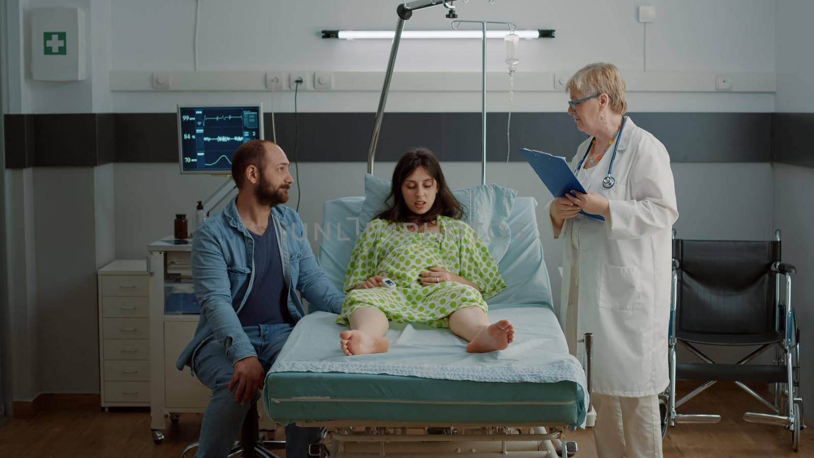 Caucasian pregnant person getting advice from doctor while sitting with husband in hospital ward. Young woman expecting child at maternity clinic. Obstetrics specialist consulting patient
