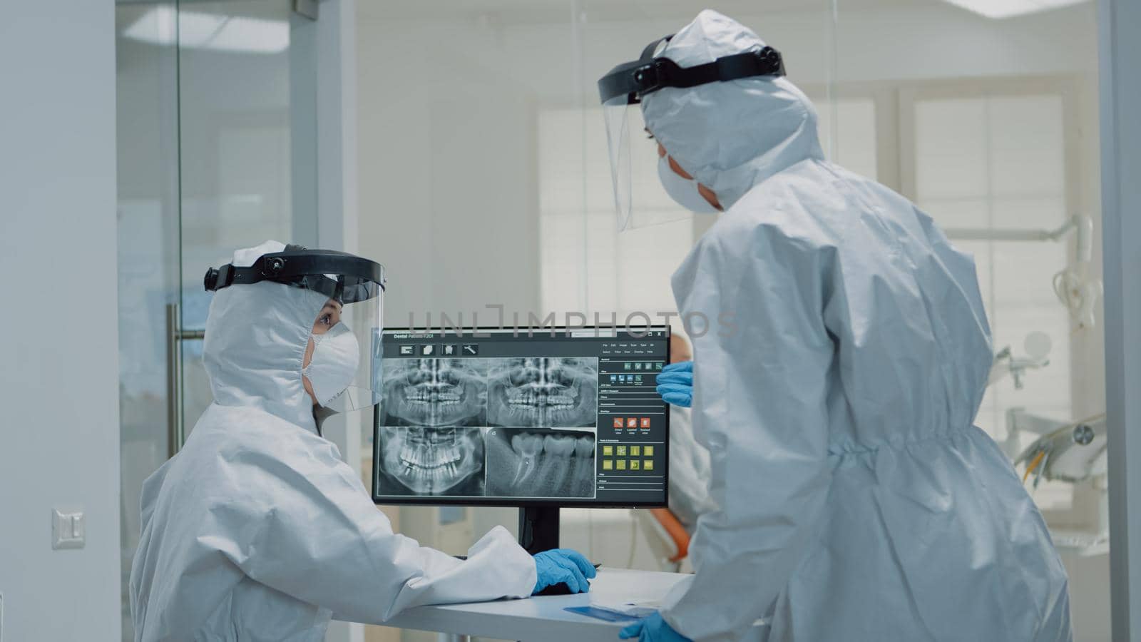 Professional dentistry staff with ppe suit looking at teeth x ray by DCStudio