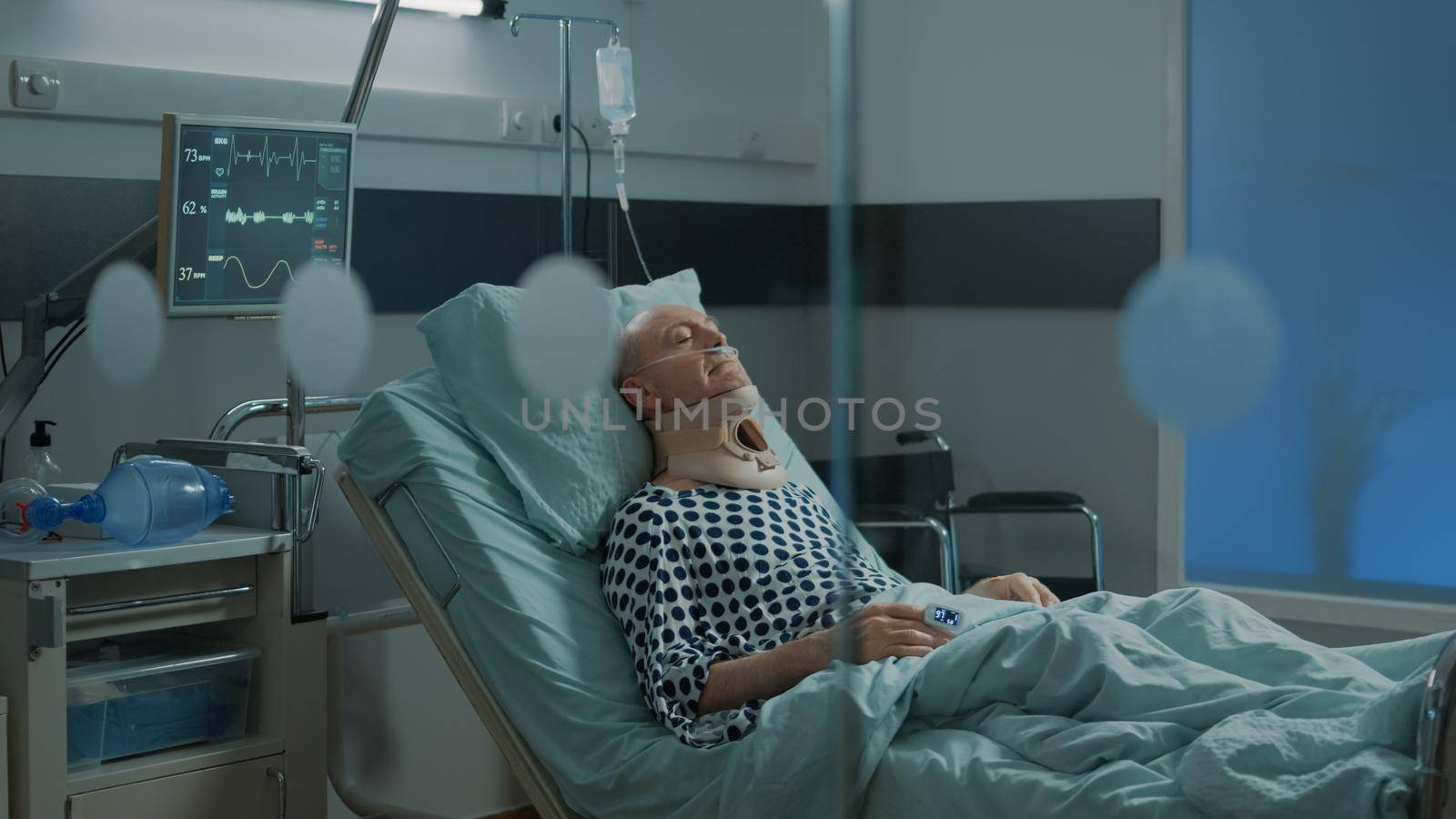 Sick patient recovering from injury with cervical collar for neck in hospital ward at medical unit. Old man in modern intensive care room sitting in bed with oximeter and oxygen tube