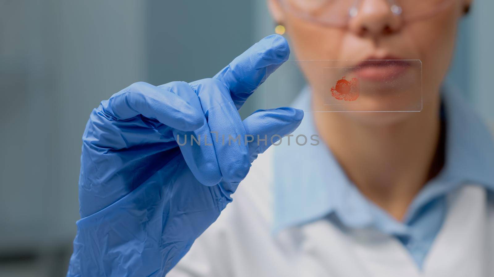 Close up of hand holding glass tray with blood for test experiment in science laboratory. Doctor with gloves analyzing dna sample on microbiology tool for professional medical diagnosis