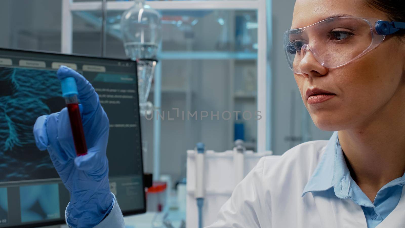 Close up of scientist analyzing lab vacutainer with fluid in laboratory. Woman with chemical equipment holding glass flask for blood cell examination. Transparent tube with solution