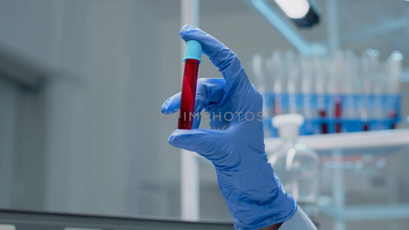 Close up of glass vacutainer filled with dna solution for test in chemical laboratory. Doctor hands with gloves holding transparent sample flask with fluid blood for lab analysis