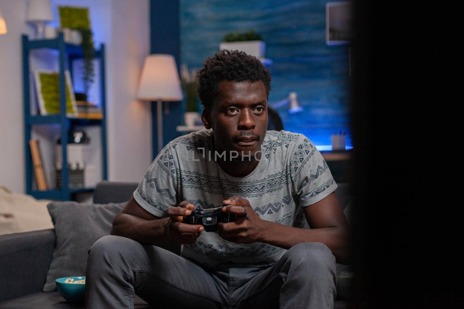 African american gamer young man holding gaming controller playing online videogames on television during soace shoother competition. Black guy enjoying relaxing alone at home. Virtual game