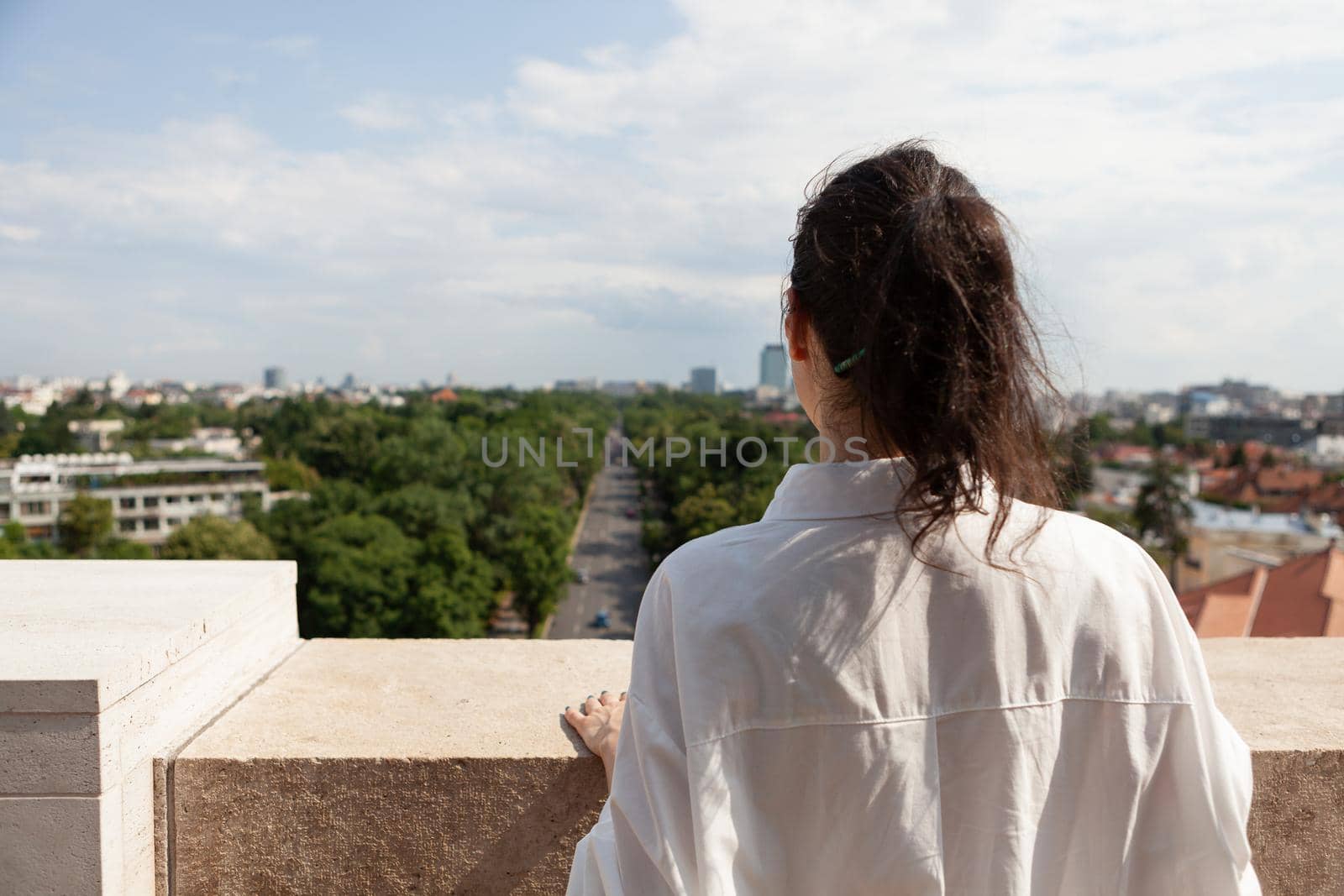 Woman tourist standing on tower terrace enjoying summer vacation looking at panoramic view of metropolitan city. Landscape with urban buildings seeing from rooftop observation point. Travel concept