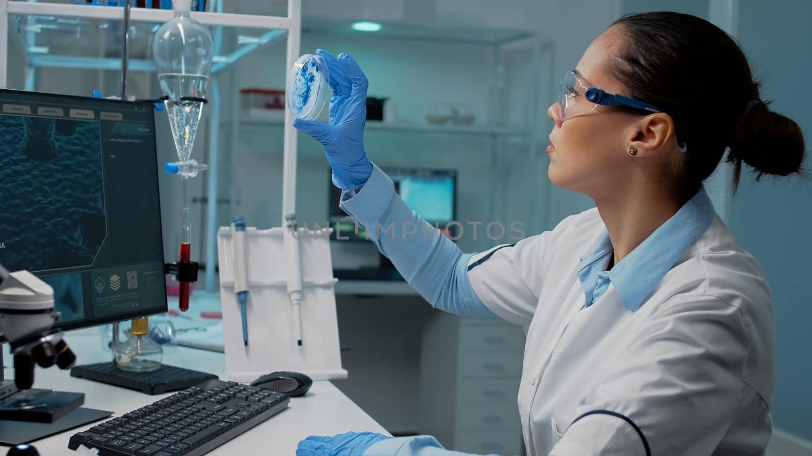 Scientist in laboratory analyzing petri dish with liquid bacteria while typing on computer with dna animation. Chemistry doctor with lab equipment working on genetic microbiology