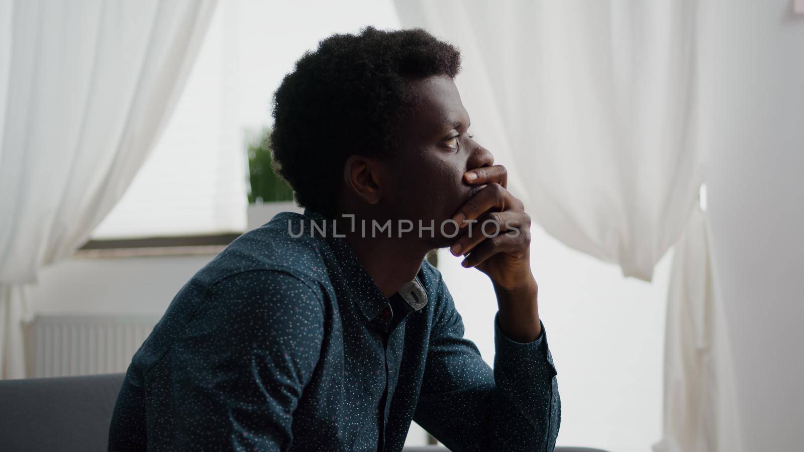 Portrait of pensive thoughtful african american man looking out the window, dreaming or thinking at problems. Adult black man in living room from home office