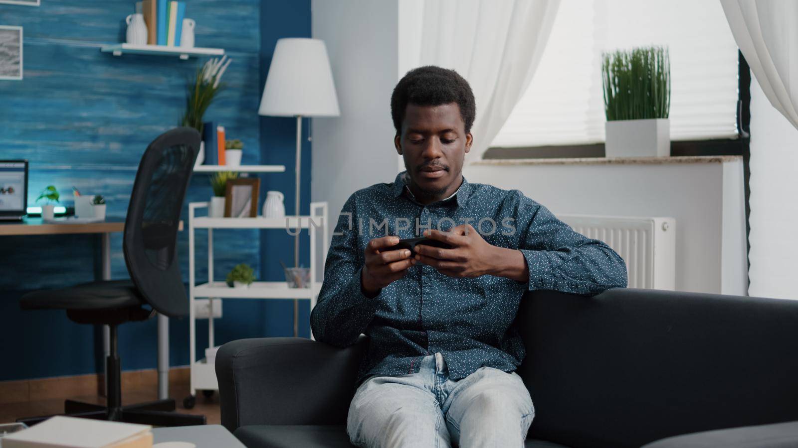 African american man playing video games on his phone, lying in bed, using internet wirelles internet connection. Gamer on smartphone technology working