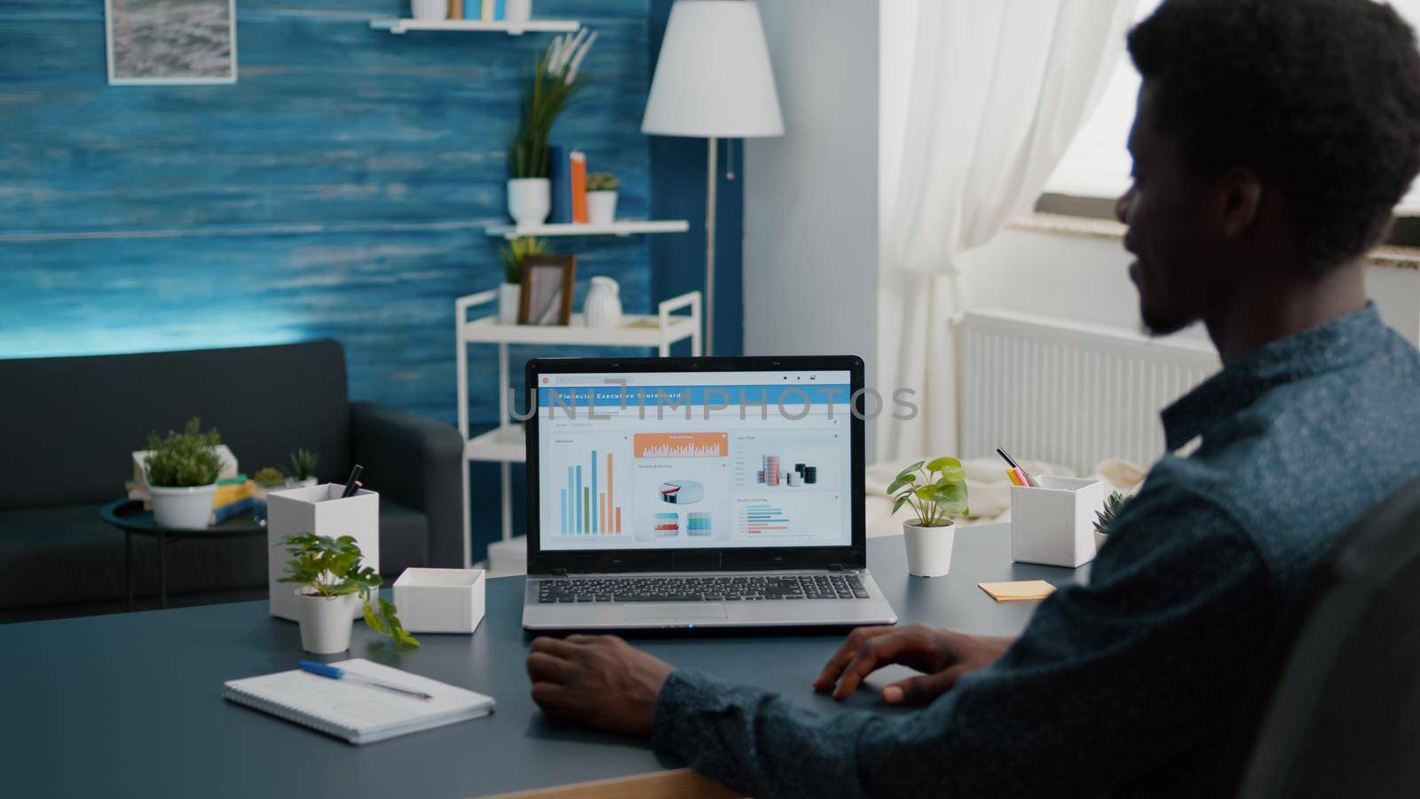 Black man working from home, remote working from living room using financial economy data app on laptop. African american guy computer user using business internet online web communication job interface