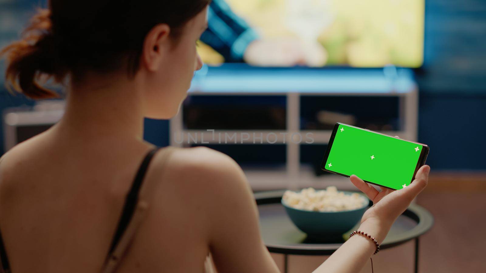 Person holding modern phone with horizontal green screen for chroma key and copy space with isolated background. Young woman sitting at home with equipment and mockup layout for template