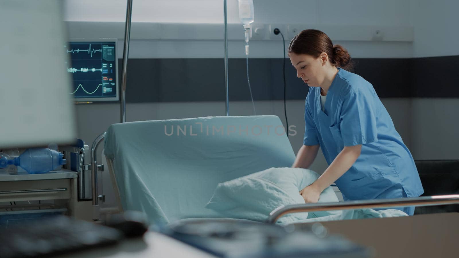 Medical nurse preparing hospital ward bed with pillow and blanket for comfort of sick person. Intensive care unit filled with modern medical equipment for disease treatment, surgery recovery