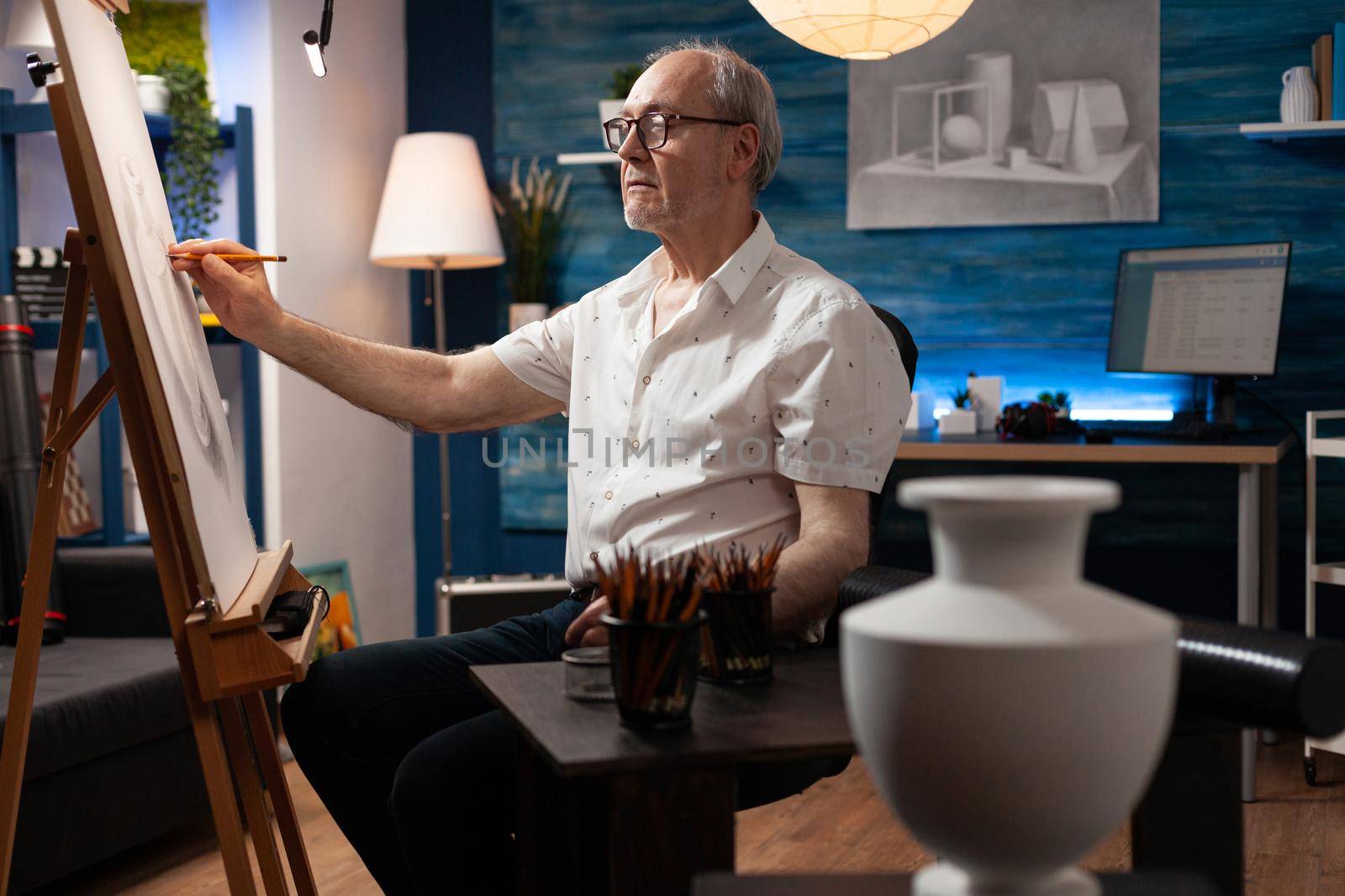 Elderly artist working on vase drawing with pencil on canvas and easel in artwork studio at home. Senior creative person creating masterpiece for fine art project with professional tools