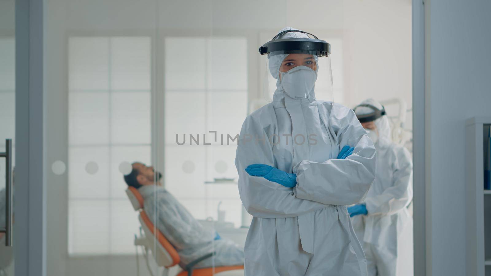 Portrait of caucasian dentist prepared for dental surgery at oral clinic, wearing protection suit with mask, face shield, gloves and coverall. Stomatology specialist looking at camera