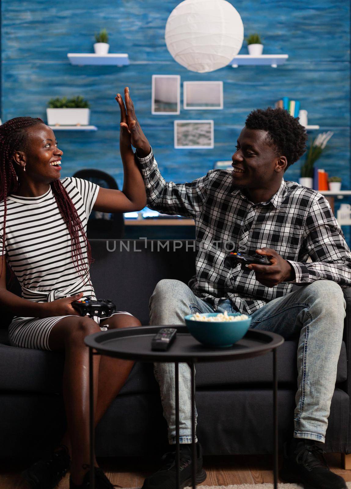 African american couple highfive after winning activity on TV at home. Black partners playing video game on television with console, holding controllers and feeling happy about win