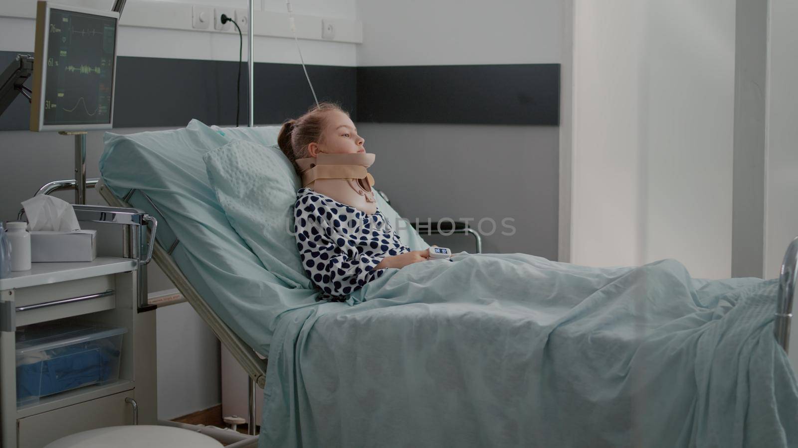 Sick patient resting in bed wearing neck cervical collar having health injury recovering after painful sickness surgery. Little child wearing oxygen nasal tube during rehabilitation in hospital ward