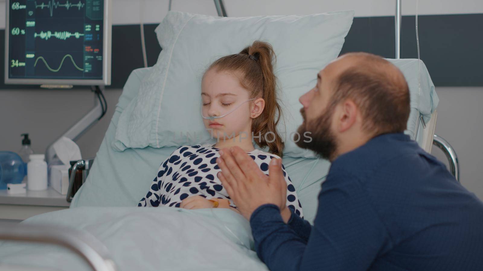 Sick daughter sleeping while worried sad father praying for heath care recovery by DCStudio