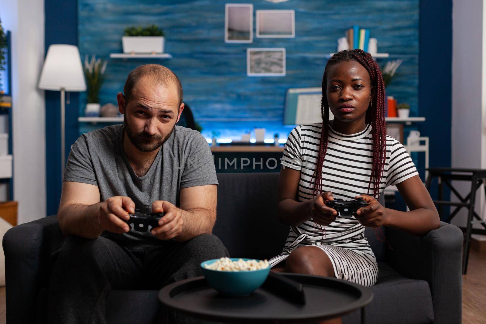 POV of interracial couple playing video game on console holding joysticks at television. Multi ethnic partners looking at camera while enjoying fun activity with technology and controllers