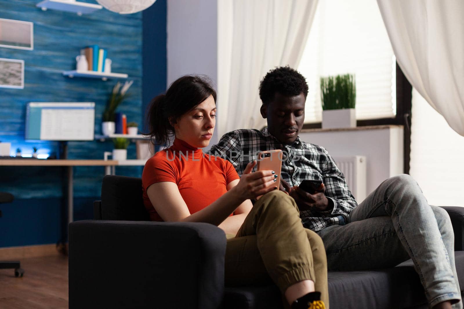 Interracial couple sitting on couch relaxing at home by DCStudio